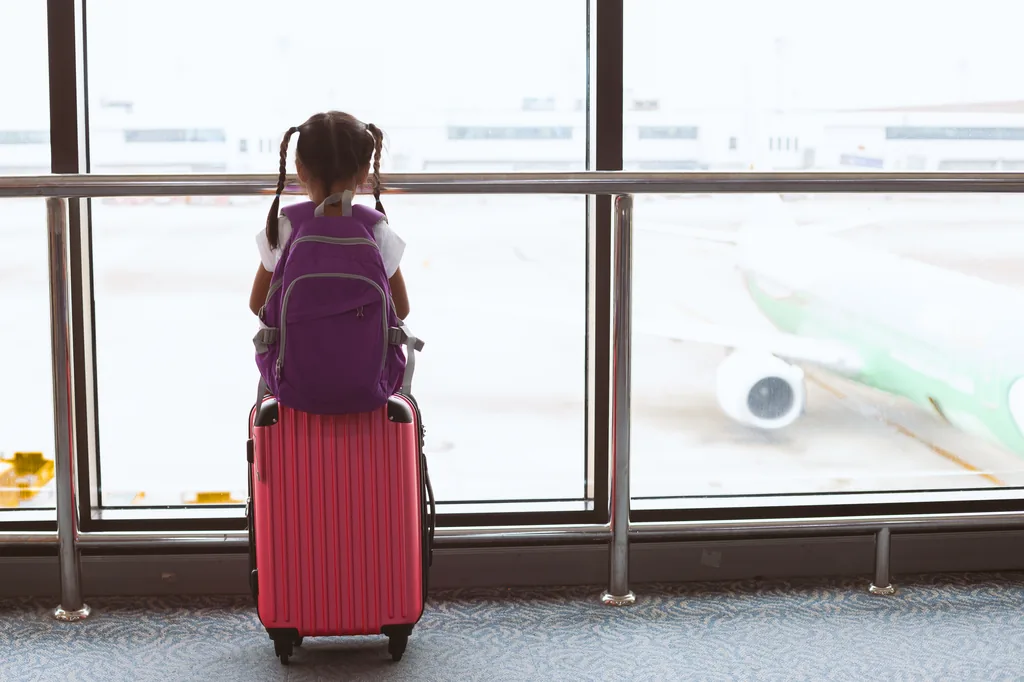 Bé gái háo hức kéo vali nhìn ra máy bay tại sân bay trước chuyến về Việt Nam