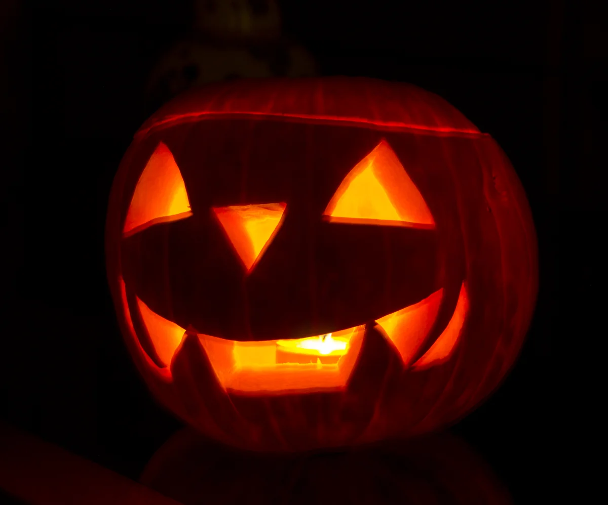 Đèn bí ngô Halloween có mắt và miệng khắc sáng trên nền tối
